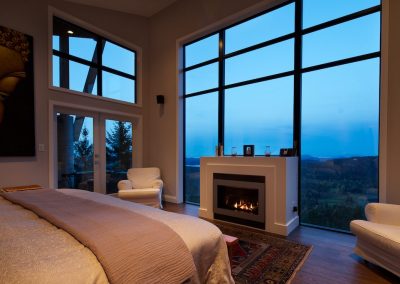 Bedroom with a fireplace and tall windows at dusk